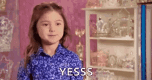 a little girl in a blue shirt is standing in front of a shelf with a shelf full of trophies .