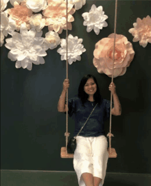 a woman is sitting on a swing in front of flowers on the wall