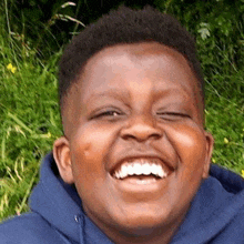 a young boy wearing a blue hoodie is laughing with his eyes closed .