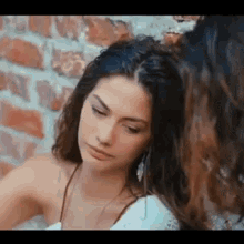 a woman is sitting next to another woman in front of a brick wall and looking at the camera .