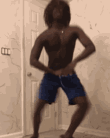 a shirtless man in blue shorts is standing in front of a door .