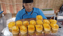 a man in a blue shirt is looking at a bunch of cakes on a tray with the words made in animotica below him