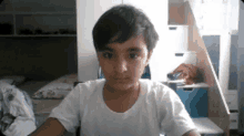 a young boy in a white shirt looks at the camera in a bedroom