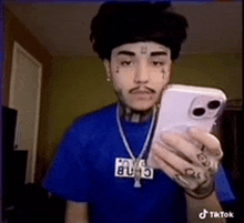 a man wearing a blue shirt and a necklace is taking a selfie with his phone .