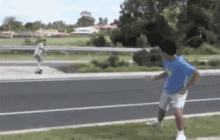 a man is playing soccer on the side of the road while another man is riding a skateboard down the road .