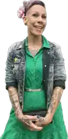 a woman wearing a green dress and a denim jacket has a tattoo on her arm