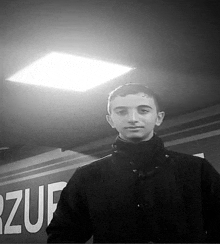 a young man in a black jacket is standing in front of a sign in a black and white photo .