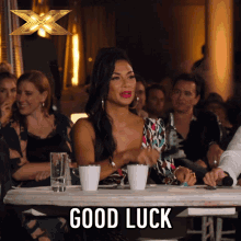 a woman sits at a table with two cups of coffee and a sign that says good luck on it