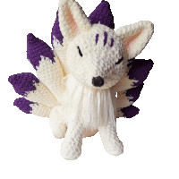 a stuffed animal with purple ears and tail is sitting on a white surface