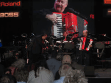 a man is playing an accordion in front of a roland boss banner