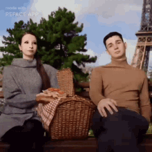 a man and a woman are sitting next to each other with a picnic basket in front of the eiffel tower