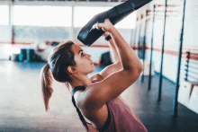 a woman in a pink tank top is lifting a black object over her head