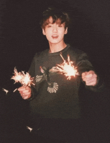 a young man in a black sweater holding sparklers in his hands