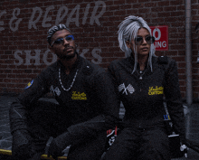 a man and a woman are sitting in front of a sign that says repair shops