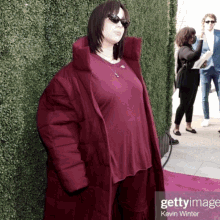 a woman wearing sunglasses and a burgundy coat is standing on a red carpet with the caption getty image kevin winter