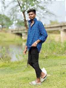 a man wearing a blue plaid shirt and black pants is standing in a field