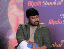 a man is sitting in front of a bhola shankar sign