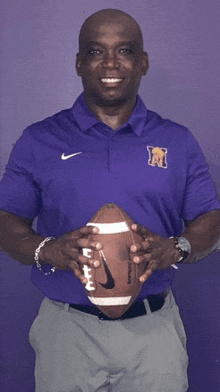 a man in a purple nike shirt holds a football in his hands