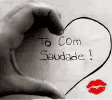 a black and white photo of a hand making a heart with the words `` to com saudade '' written on it .