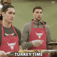 two men wearing red aprons with bulls on them are holding a tray of food with the words turkey time below them