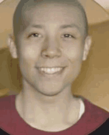 a young man with a shaved head is smiling and wearing a red t-shirt .