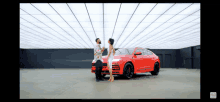 a man and woman standing next to a red car