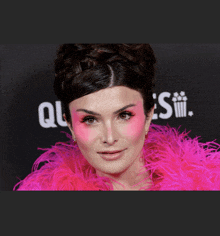 a woman with pink paint on her face is wearing a bright pink feathered jacket