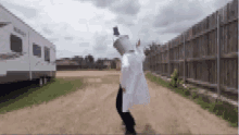 a man in a white coat stands on a dirt road in front of a trailer that says rv on it