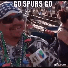 a man wearing a hat , sunglasses , beads and a microphone with the words `` go spurs go '' on it