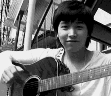 a young man is holding an acoustic guitar and smiling in a black and white photo .