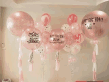 a bunch of pink balloons with happy birthday written on them are hanging from a wall .