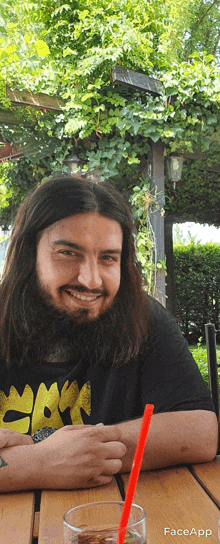 a man with long hair and a beard is sitting at a table with a glass and a straw in front of him