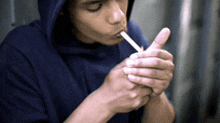 a man in a hoodie is lighting a cigarette