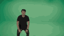 a man in a black shirt is squatting in front of a green screen .