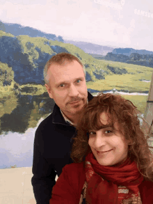 a man and a woman are posing in front of a painting of a river