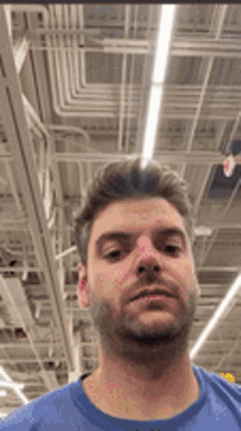 a man in a blue shirt is taking a selfie in a store with a ceiling in the background .