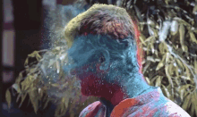 a man is covered in blue and red powder while standing in front of a tree