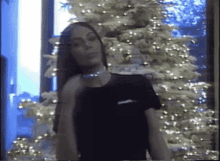 a woman is standing in front of a christmas tree wearing a black shirt .