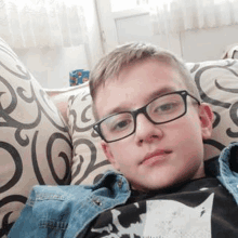 a young boy is laying on a couch wearing glasses and a denim jacket .