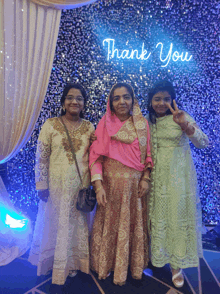 three women posing for a picture in front of a thank you sign