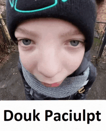 a young boy wearing a black hat and scarf looks at the camera with the words douk paciulpt above him