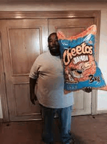 a man is holding a bag of cheetos in front of a door .