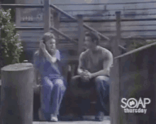 a man and a woman are sitting next to each other on a porch talking on a cell phone .