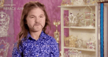 a man with long hair and a beard wearing a blue shirt is standing in front of a shelf full of tiaras .