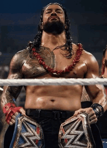 roman reigns is standing in a wrestling ring holding two championship belts .