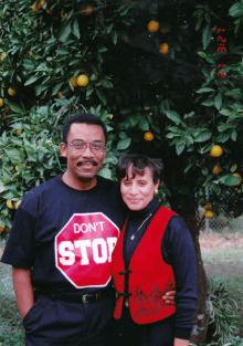 a man wearing a black shirt that says " do n't stop " stands next to a woman wearing a red vest