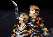 a man and a woman are dressed as cats and one of them is raising her hand