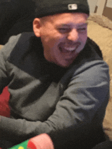 a man wearing a black hat and a grey sweater is laughing