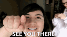 a woman with braces on her teeth is pointing at the camera with the words " see you there " below her