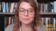 a woman wearing glasses and ear buds stands in front of a bookshelf with holy post written on the bottom